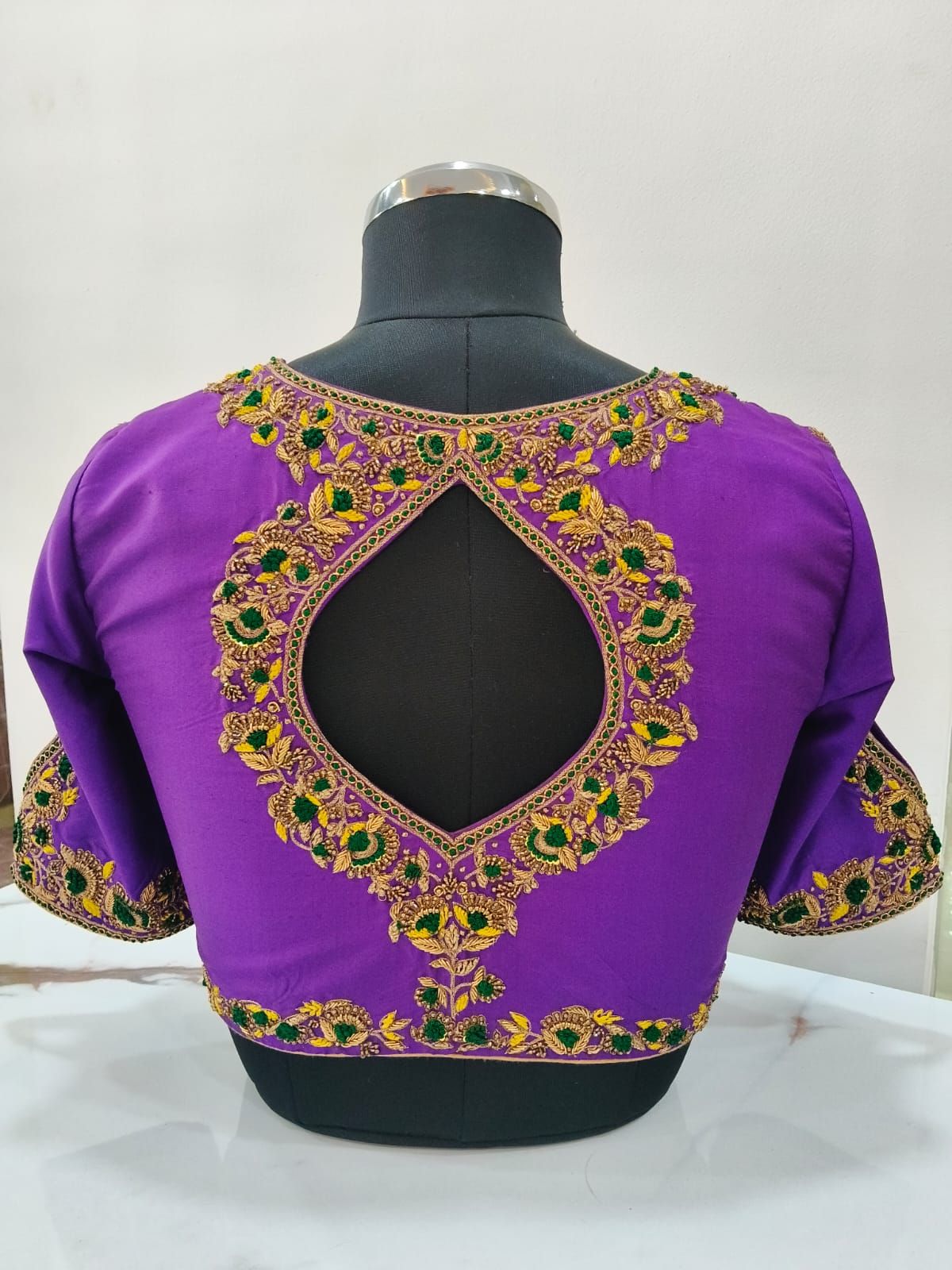Violet blouse back with a teardrop keyhole outlined in gold and green aari work