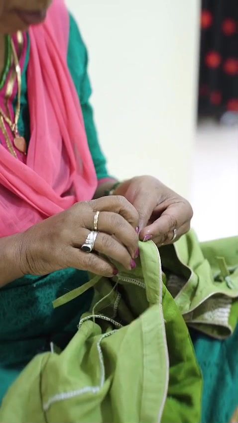Hands finishing a green garment with needle and thread